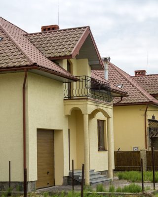 New yellow two-story residential cottage with shingle roof, front porch, plastic windows, high chimneys, balconies on blue sky background. Real estate property, architecture and prosperity concept.